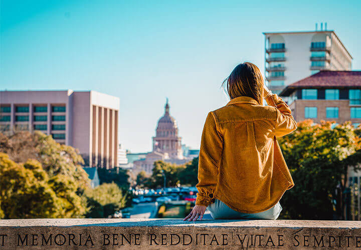 Person sitting on wall looking toward Texas state capitol building in Austin