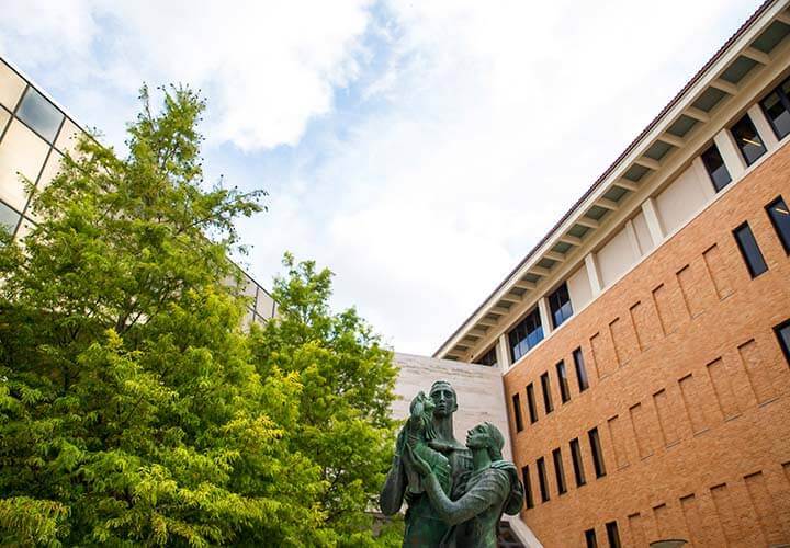 McCombs family statue under a tree against the GSB building