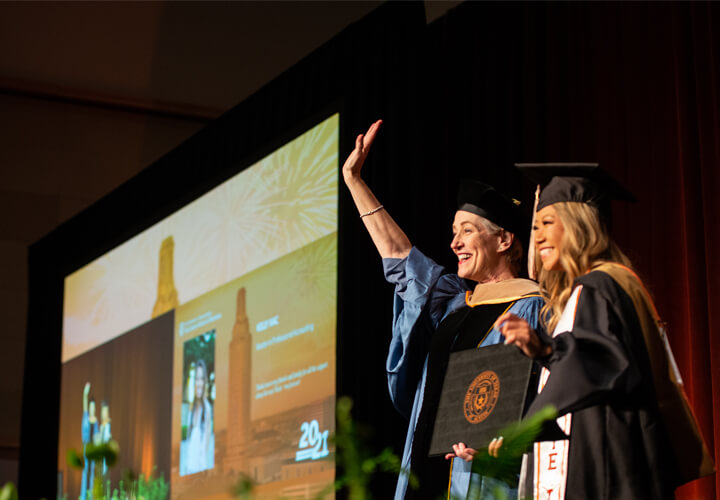 Dean Mills waves on stage while presenting graduate with diploma