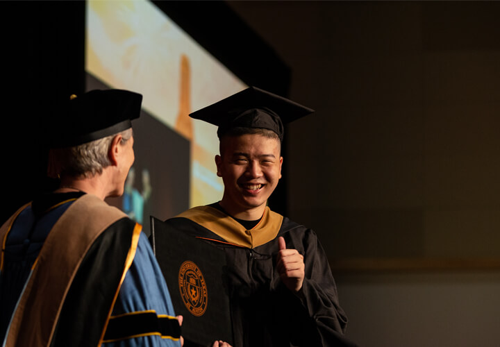 Smiling graduate on stage with Dean Mills