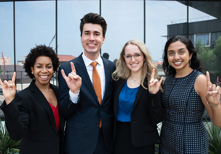 Four business casual students give hook em horns