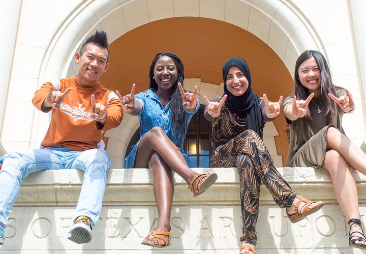 Four students sitting on bench and giving hook em horns