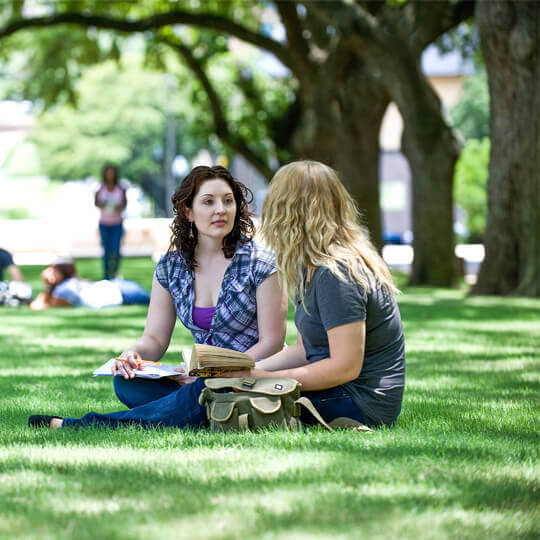 Students sitting on the west mall under trees.